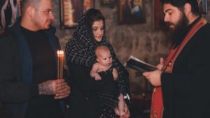 A touching moment during an Orthodox baptism ceremony with a priest, parents, and baby.